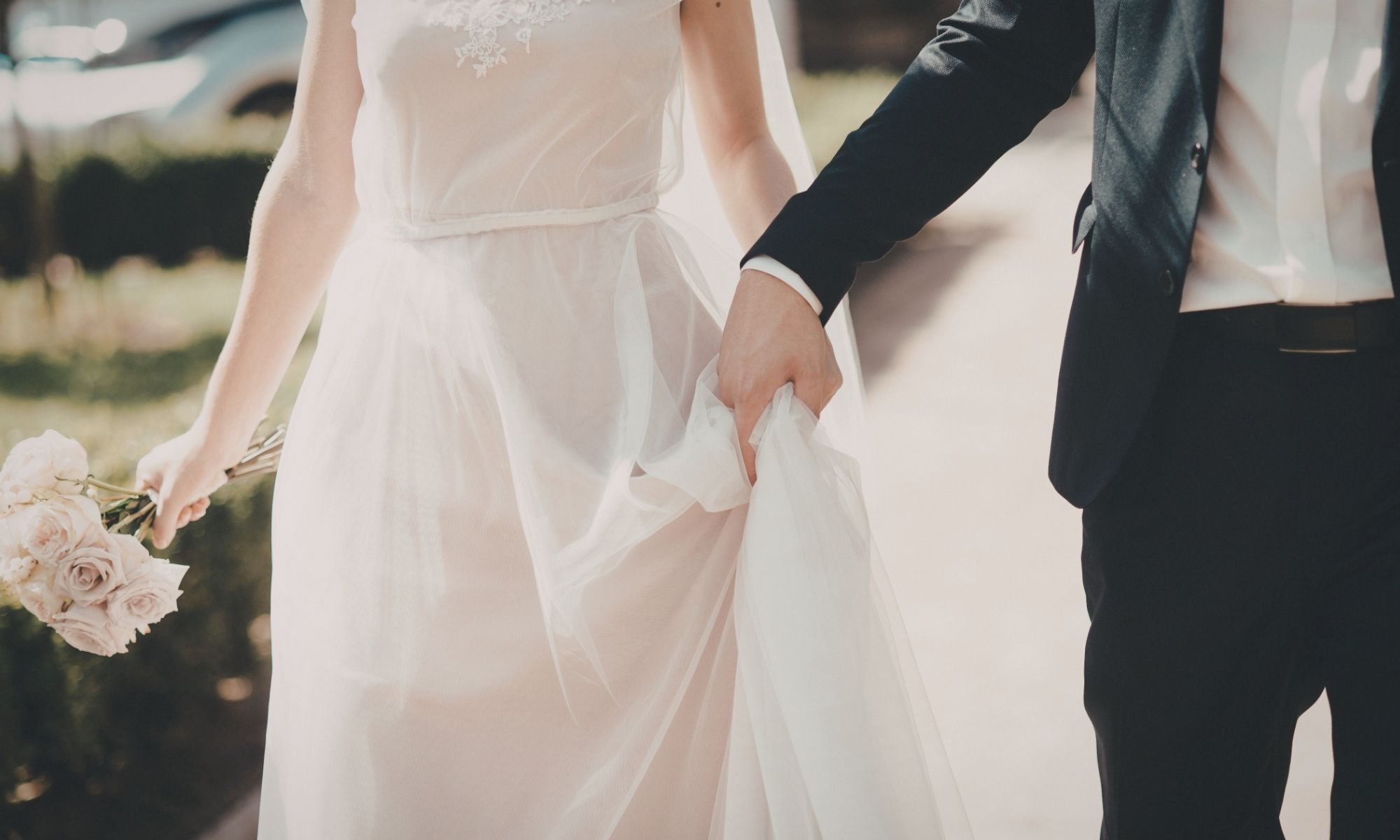 Bride in white dress holds bouquet and partner’s hand outdoors—a beautiful Kathy Rozmeta Celebrant moment.